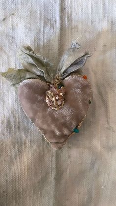 a heart shaped brooch sitting on top of a white cloth covered table next to a wall