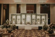 an indoor wedding setup with white flowers and greenery on the wall behind the altar