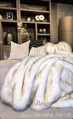 a large white fur blanket sitting on top of a bed next to a book shelf