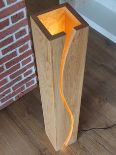 a wooden floor lamp with an orange light in the center and a brick wall behind it