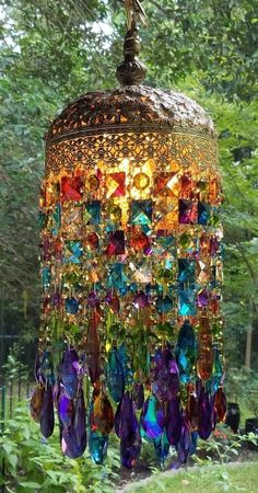 a colorful chandelier hanging from the ceiling in a garden with lots of trees