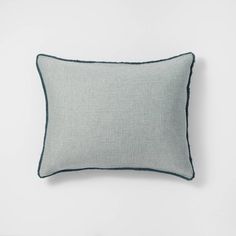 a gray pillow with black piping on the front and back, against a white wall