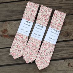 three ties are laid out on a wooden surface, one is pink and the other is white