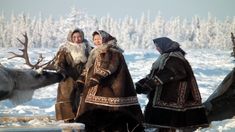 three people dressed in traditional clothing standing next to a reindeer