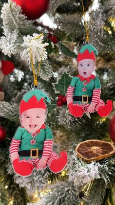 two christmas ornaments hanging from the tree in front of a christmas tree with red and green decorations