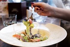 a person is cutting into a salad on a white plate with silverware in front of them