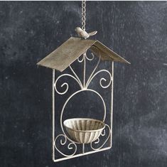 a metal bird feeder hanging from a chain with a bowl on it's side