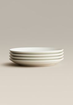 four white plates stacked on top of each other in front of a gray background,