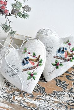 two white hearts with birds on them sitting next to a pine branch and christmas tree