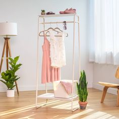 a white rack with clothes and shoes on it next to a potted plant in front of a window