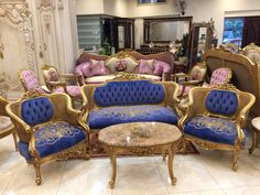 a living room filled with lots of blue and gold furniture next to a mirror on the wall