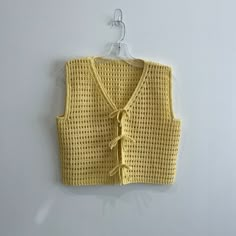 a yellow knitted vest hanging on a white wall