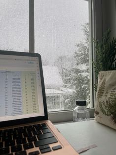 a laptop computer sitting on top of a desk next to a window covered in snow