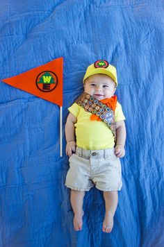 a baby wearing a yellow shirt and tie laying on a blue blanket next to a red flag