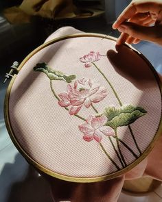 a woman is holding a cross - stitched pink flower with green leaves on it