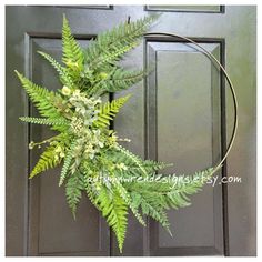 a fern wreath on the front door of a house with green paint and gold trim