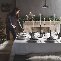 a woman standing in front of a table set for christmas dinner with candles on it