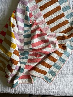 a multicolored quilt is laying on top of a white bed sheet with an orange, pink, blue, and yellow striped design