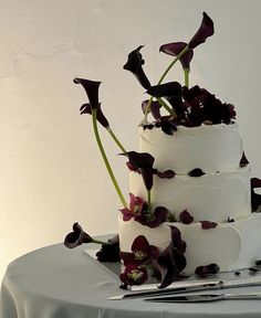 a three tiered cake with purple flowers on top and silverware next to it