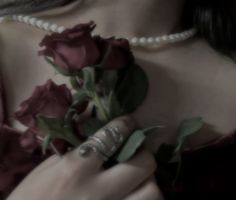 a close up of a person holding flowers with pearls on the neck and bracelets