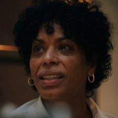 a close up of a person wearing earrings and a white shirt with black curly hair