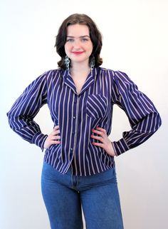 "This is a marvelous 1970s vintage blouse that has a lot going for it! The fabric is a silken poly with a very pleasant soft matte hand, like a charmeuse. The pattern is a classic vertical bar stripe in navy blue with taupe and a bright red pinstripe. It has shirring at the front shoulder yokes, puffed shoulders with small shoulder pads, long sleeves with notched single button cuffs, an open V neckline with a notched collar, and it looks great tied in front or worn with the straight hem down. Ou Vintage Blouse With Striped Collar For Spring, Retro Tops With Striped Collar For Work, Retro Workwear Tops With Striped Collar, Retro Striped Tops For Work, Spring Vintage Blouse With Striped Collar, Vintage Spring Blouse With Striped Collar, Retro Fitted Striped Blouse, Vintage Striped Tops With Buttons, Vintage Long Sleeve Tops With Striped Collar