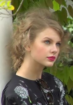 a close up of a person wearing a black shirt and red lipstick with trees in the background