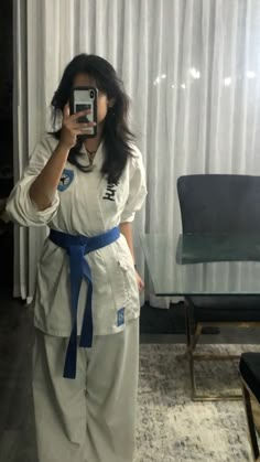 a woman taking a selfie in front of a mirror wearing a karate outfit and holding a cell phone