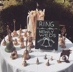 a table topped with lots of brass bell decorations and a sign that says ring the newly weds