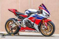 a red, white and blue motorcycle parked next to a wall