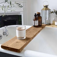 a candle and some bottles are sitting on a wooden shelf in front of a bathtub