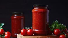 tomato sauce in a jar surrounded by tomatoes and parsley on a cutting board with two jars next to it