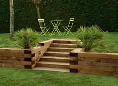 a garden with wooden steps leading up to the grass area and two chairs in the background