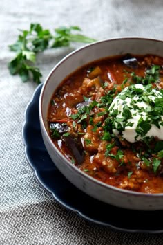 a bowl of chili with sour cream and parsley in it on a blue plate