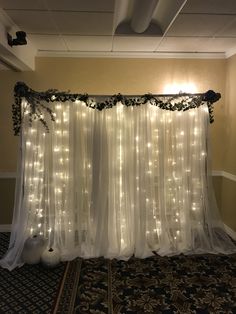 a white curtain with lights on it in front of a carpeted floor and wall