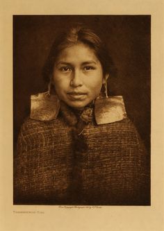 an old black and white photo of a woman with large earrings on her head, looking at the camera