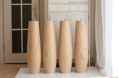 three tall wooden vases sitting next to each other on a white floor in front of a cabinet