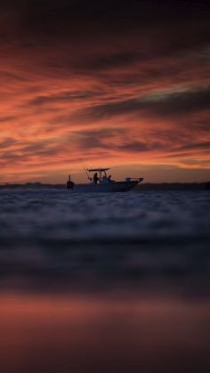 a fishing boat is silhouetted against an orange and pink sky as it sits in the ocean