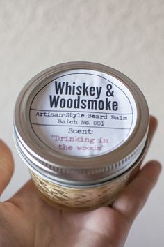 a person holding a jar of whiskey and woodsmoke in their left hand with the label on it