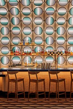 a bar with several chairs and bottles on the wall behind it in front of circular glass windows