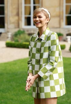 a woman in green and white checkered coat standing on the grass with her hands together