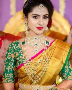 a woman in a green and gold sari with jewelry on her neck, holding a red