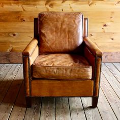 a brown leather chair sitting on top of a wooden floor next to a wood wall