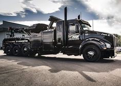 a large black truck parked in a parking lot next to a tall building and cloudy sky