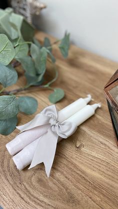 a white candle with a bow on it sitting on a table next to some leaves