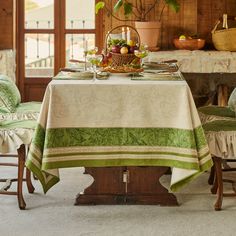 a dining room table set with green and white linens, fruit on top of it