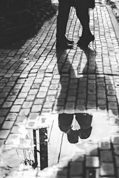 a person walking down a sidewalk with an umbrella over their head and reflection in the water