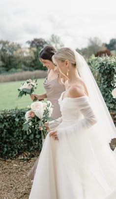 two women in wedding gowns standing next to each other and one is holding a bouquet