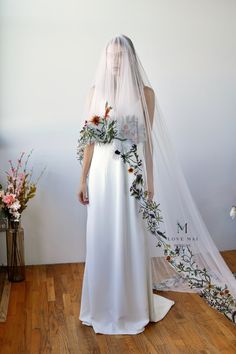 a woman in a white wedding dress with flowers on the side and a veil over her head