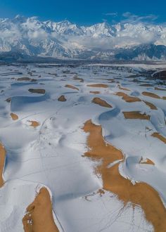 an aerial view of snow covered ground with mountains in the distance and blue sky above